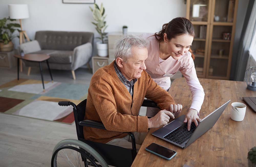 support worker helps disabled man with laptop